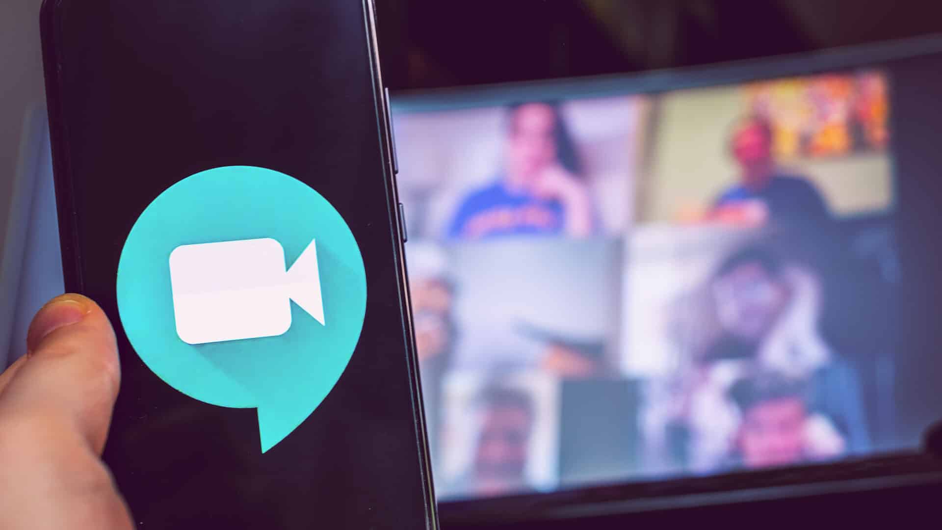 Google Meet Logo auf einem Smartphone, im Hintergrund Kachelansicht einer Videokonferenz auf Desktop